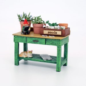 May include: A green wooden potting bench with a cat sitting on the lower shelf. There is a small gnome figurine sitting on the top shelf, along with a wooden box labeled "seeds" and several potted plants.