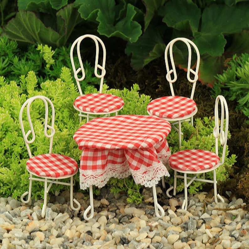 May include: A miniature white metal table and four chairs with red and white checkered fabric seats and tablecloths. The set is on a bed of white gravel.