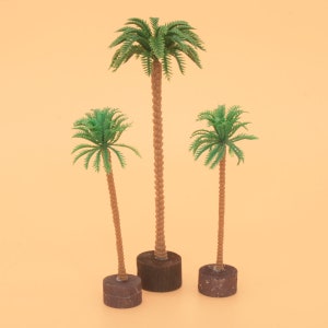 Può includere: Tre palme in miniatura di plastica con tronchi marroni e fronde verdi. Gli alberi sono su basi marroni.