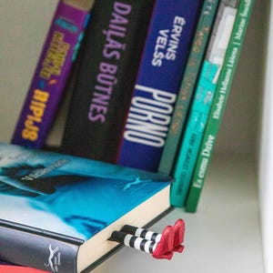 A black bookmark shaped like the Wicked Witch of the West's legs, complete with red shoes and striped stockings, sticking out from  books on a shelf.