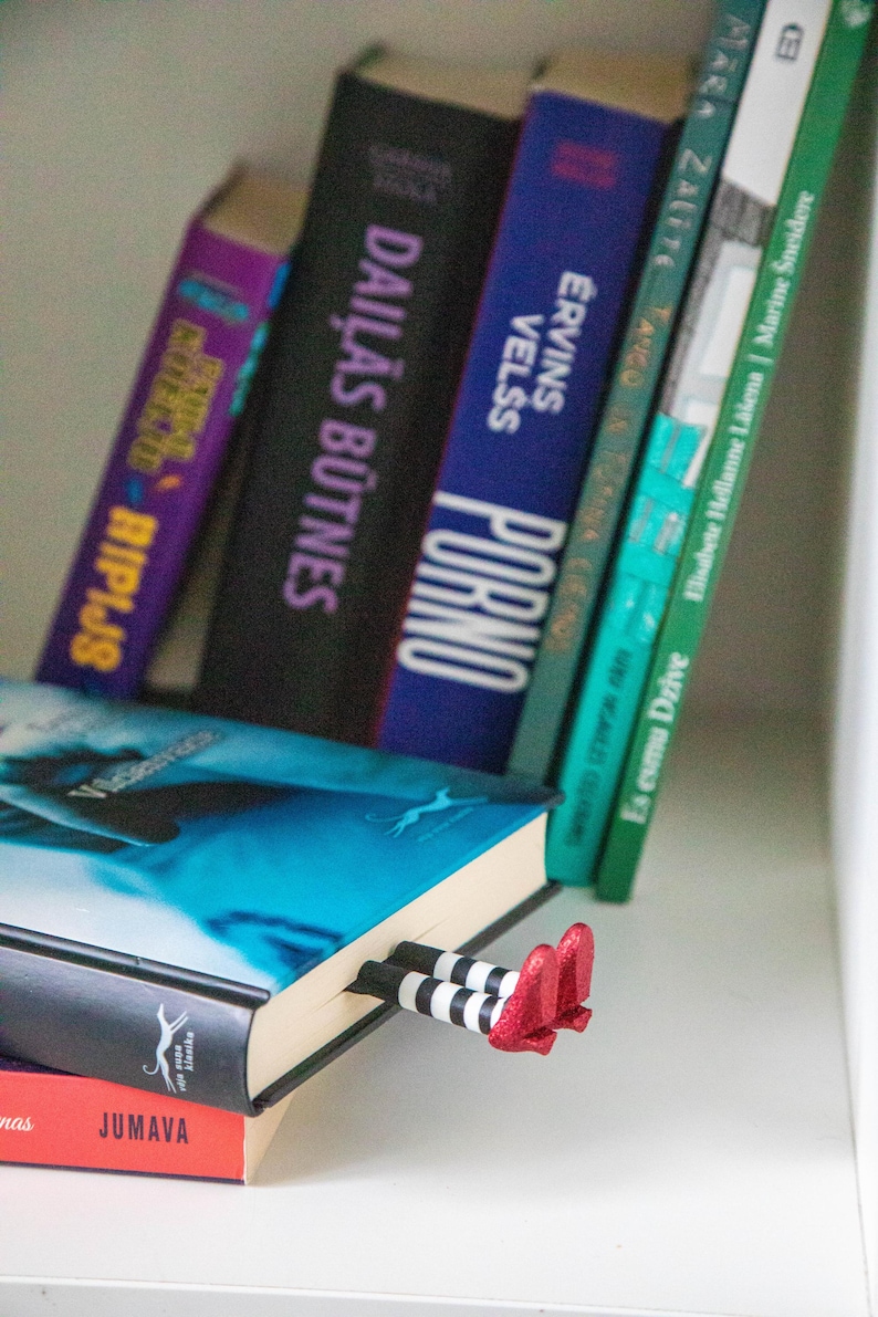 A black bookmark shaped like the Wicked Witch of the West's legs, complete with red shoes and striped stockings, sticking out from  books on a shelf.