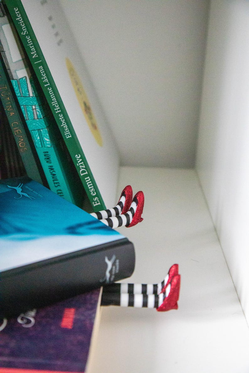 A black bookmark shaped like the Wicked Witch of the West's legs, complete with red shoes and striped stockings, sticking out from  books on a shelf.