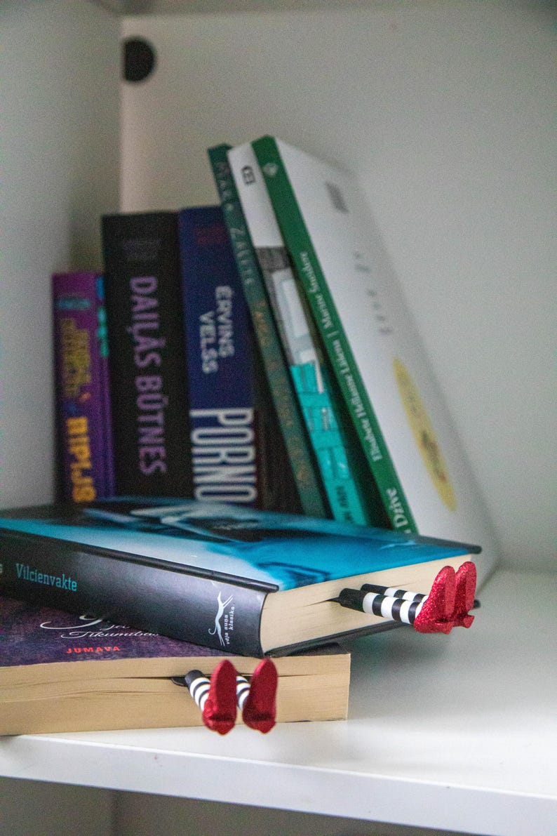 A black bookmark shaped like the Wicked Witch of the West's legs, complete with red shoes and striped stockings, sticking out from  books on a shelf.