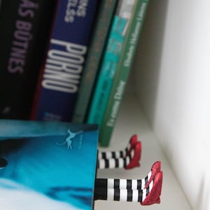 A black bookmark shaped like the Wicked Witch of the West's legs, complete with red shoes and striped stockings, sticking out from  books on a shelf.