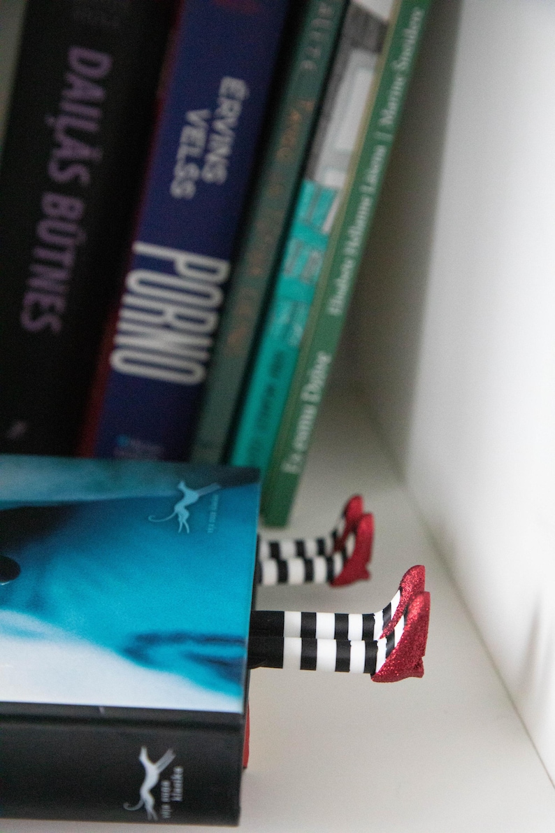 A black bookmark shaped like the Wicked Witch of the West's legs, complete with red shoes and striped stockings, sticking out from  books on a shelf.