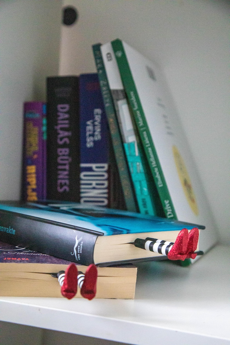 A black bookmark shaped like the Wicked Witch of the West's legs, complete with red shoes and striped stockings, sticking out from  books on a shelf.