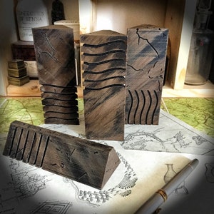 Peut inclure: Quatre blocs en bois avec des motifs sculptés différents. Les blocs sont brun et noir avec une finition vieillie. Les blocs sont disposés sur une surface blanche avec une carte et un stylo.
