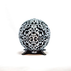 May include: A black and silver sphere with a decorative, intricate pattern. The sphere is on a black stand.