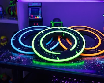 May include: Three glowing, circular objects with black and neon accents are displayed on a table. The objects have a futuristic design, with neon blue, green, and orange lights. The scene is illuminated by a purple light.