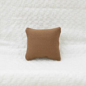 May include: A brown square pillow with a textured fabric surface.