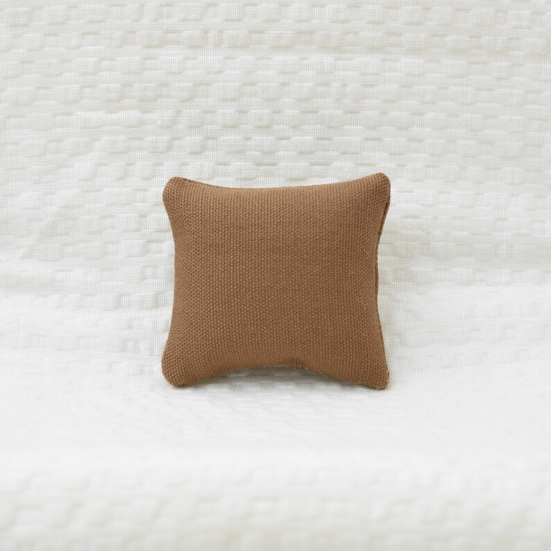 May include: A brown square pillow with a textured fabric surface.