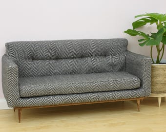 Könnte beinhalten: Ein grau-weiß gemustertes Sofa mit Holzbeinen. Das Sofa steht auf einem hellen Holzboden.