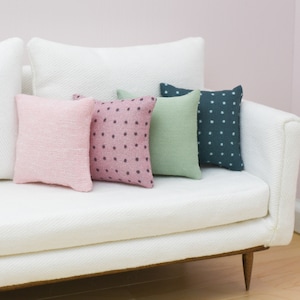 May include: A white couch with four throw pillows. The pillows are pink with white polka dots, pink with white dots, green, and dark blue with white dots.