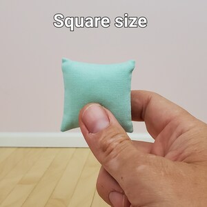 May include: A small, light blue square pillow. The pillow is being held in a hand, showing its size.