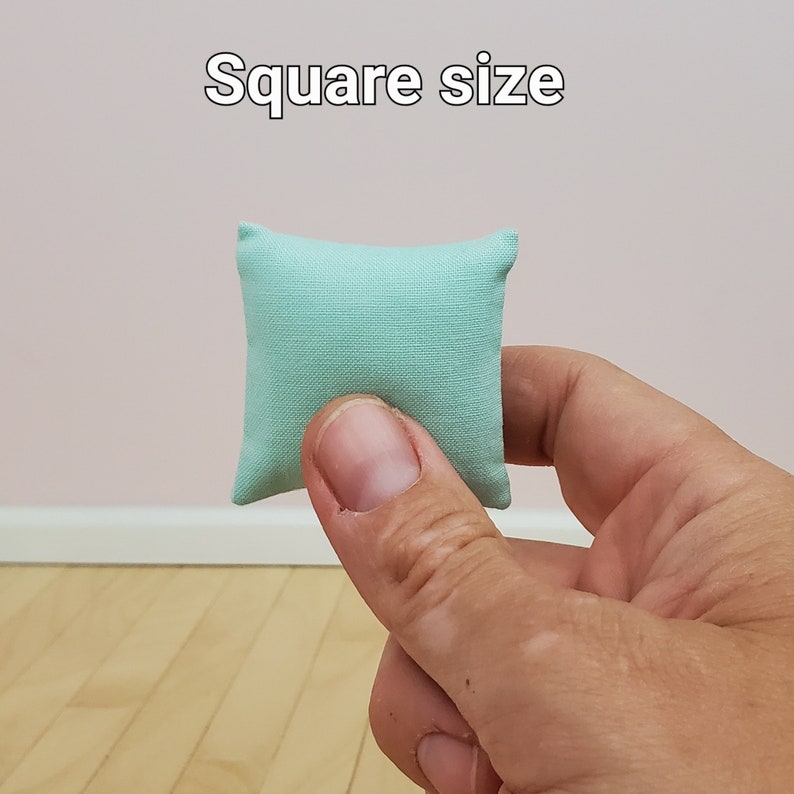 May include: A small, light blue square pillow. The pillow is being held in a hand, showing its size.