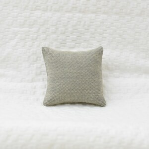 May include: A small, square, light gray throw pillow with a textured fabric.