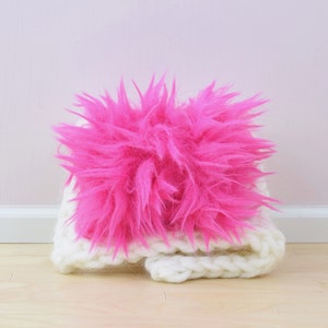 May include: A white knitted headband with a large, fluffy pink pom-pom on top.