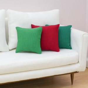 May include: Three throw pillows on a white couch. The pillows are green, red, and green. The couch is white with a textured fabric.