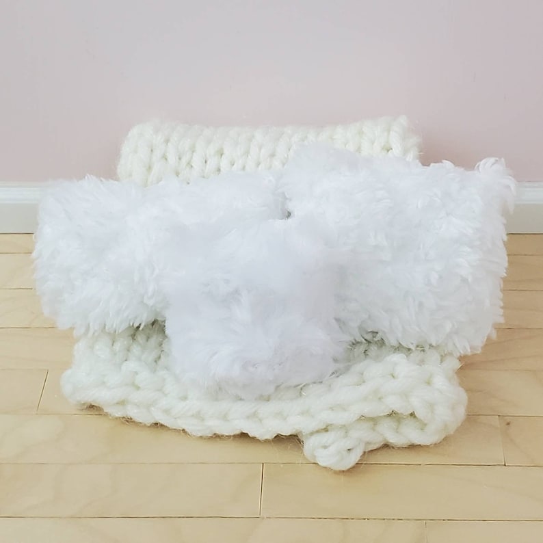 May include: Three white fluffy cushions on a white knitted throw. The cushions are soft and plush, and the throw is made of a thick, cosy yarn.