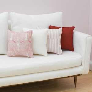 May include: A white sofa with four throw pillows. The pillows are in various patterns and colors, including pink, red, and white.