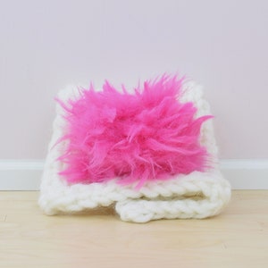May include: A white crocheted scarf with a bright pink fluffy pom-pom.