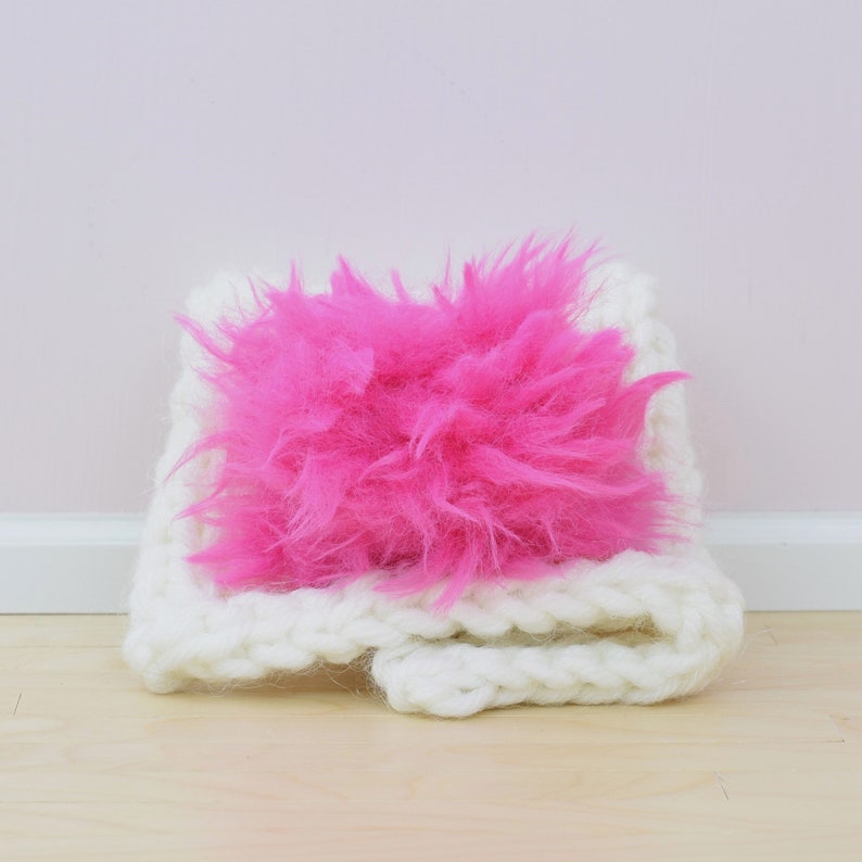 May include: A white crocheted scarf with a bright pink fluffy pom-pom.