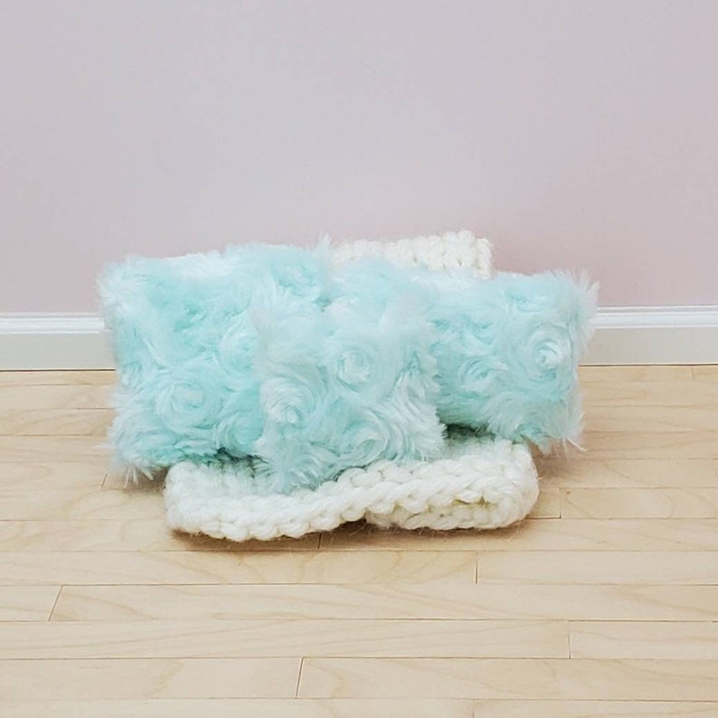 May include: Three light blue fluffy pillows with a white crocheted blanket. The pillows have a rosette pattern.