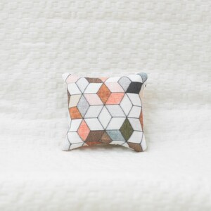 May include: A square pillow with a geometric pattern in shades of orange, brown, gray, and white.