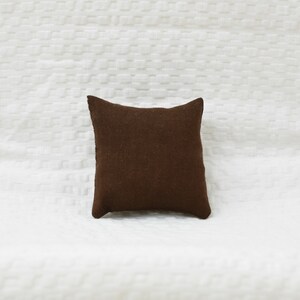 May include: A brown square pillow with a textured fabric surface.