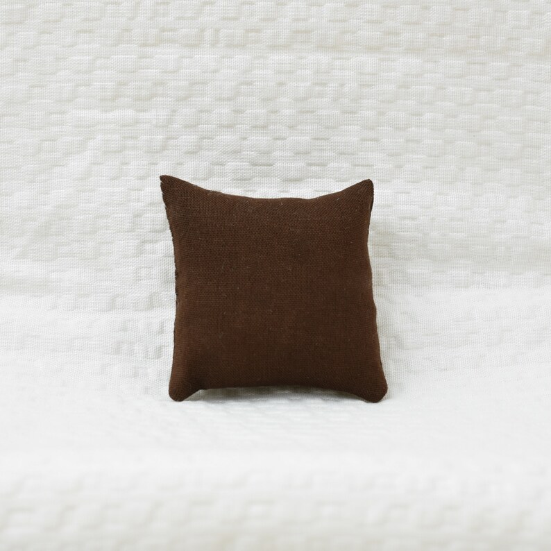 May include: A brown square pillow with a textured fabric surface.