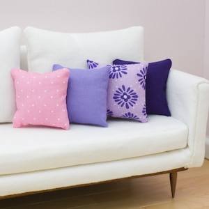 May include: A white couch with four throw pillows. The pillows are pink with white polka dots, purple, and light purple with a purple floral pattern.