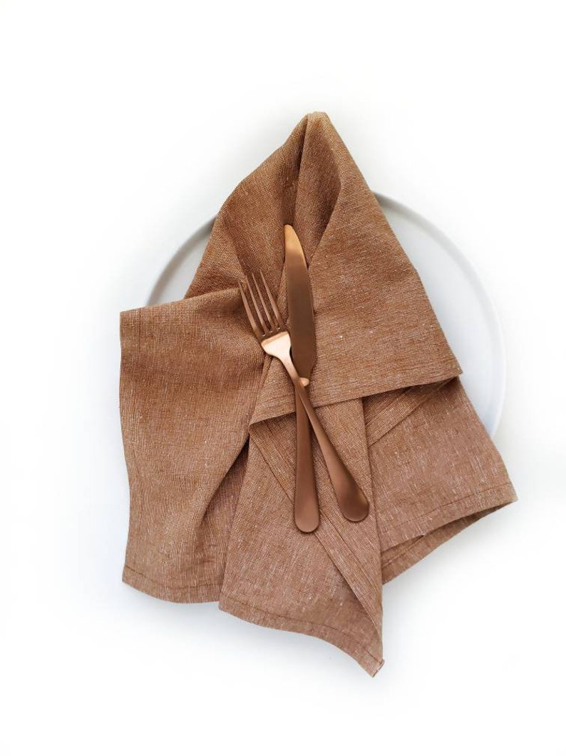 A caramel colored linen towel is shown on a white plate with coppery-colored silverware.