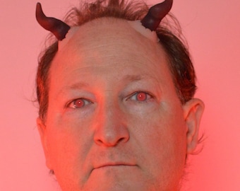Könnte beinhalten: Eine Person mit roten Augen, die schwarze Teufelshörner auf der Stirn trägt.