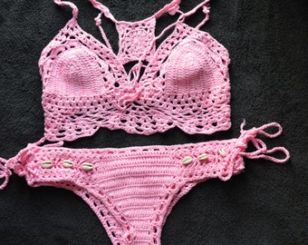 May include: A pink crochet bikini top and bottom with shell accents. The top has a criss-cross design and the bottom has a tie side. "Natali Fashion Studio" is written in white text at the top of the image.