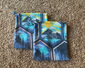 May include: Two blue fleece drawstring bags with a mountain and sun design. The bags have a honeycomb pattern and are lined with a pink fabric.