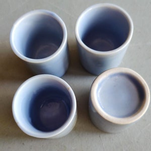 May include: Four light blue ceramic cups with a white rim. The cups are arranged in a square pattern on a light gray surface.