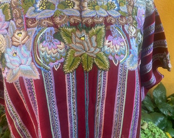 May include: A maroon blouse featuring intricate floral embroidery in shades of blue, green, and tan around the square neckline. The fabric displays vertical stripes in purple, blue, and white, with a textured weave throughout the garment.