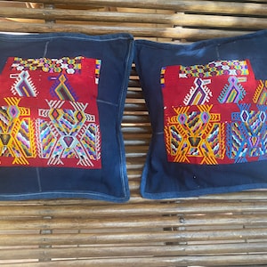 May include: Two blue and red patterned throw pillows with intricate embroidery. The pillows are made of a dark blue fabric with a red and yellow geometric design.