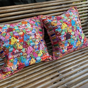 Op de afbeelding: Twee kleurrijke, geborduurde kussens met ingewikkelde patronen op een houten bank.