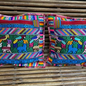 Puede incluir: Dos cojines decorativos coloridos con bordados intrincados que representan animales y pájaros. Los cojines tienen un esquema de color rojo, azul, verde, amarillo y rosa.