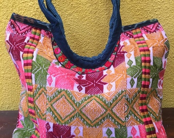 May include: A colourful woven tote bag with a blue fabric handle. The bag has a geometric pattern in shades of pink, green, orange, and white.