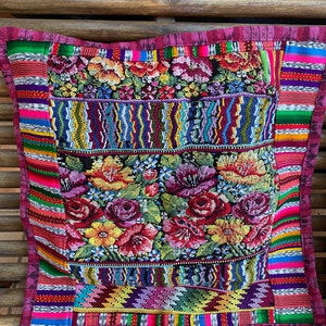 Puede incluir: Una almohada colorida con un patrón floral y diseños geométricos. La almohada está hecha de tela tejida y tiene un borde rosa.