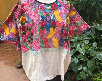 May include: A short-sleeved blouse featuring a vibrant, multi-colored woven pattern in pink, yellow, and green. The upper section is adorned with intricate floral embroidery, including blue birds and a basket motif, finished with a black neckline.