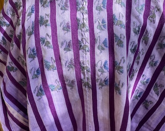 May include: A light purple and dark purple striped tunic featuring embroidered floral details around the neckline and small embroidered bird motifs scattered across the front fabric. The garment has a round neck and a vertical seam down the center.