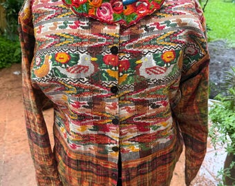 May include: A long-sleeved button-down jacket featuring a vibrant woven pattern of birds and geometric shapes in red, green, and yellow. The garment has a round neckline with a bright blue trim and a wide, colorful floral embroidered collar.