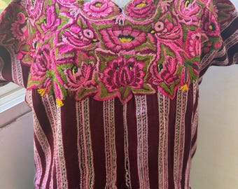 May include: A short-sleeved blouse featuring a deep maroon and light pink vertical striped pattern. The neckline and chest area are adorned with dense, vibrant pink floral and bird embroidery in shades of magenta, green, and yellow thread.