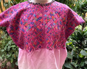May include: A vibrant, pink, embroidered tunic with a detailed geometric pattern in various colors. The top features a beaded neckline and a lighter pink, plain bottom. The garment is displayed on a mannequin.