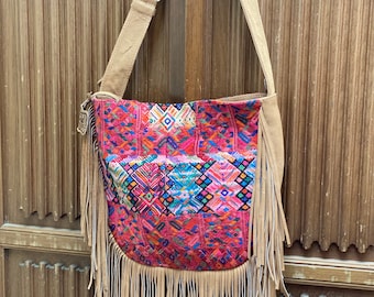 May include: A colorful, fringed, woven tapestry bag with a brown leather strap. The bag has a geometric pattern in shades of pink, red, blue, green, and yellow.