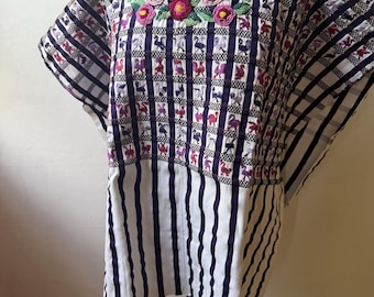 May include: A vibrant, hand-embroidered tunic top. The top features a white and purple striped pattern with a checkered design. The neckline is adorned with colorful floral embroidery. The tunic is displayed on a mannequin.