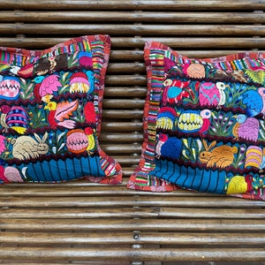 Puede incluir: Dos almohadas de tiro bordadas de colores con un fondo azul y una variedad de diseños de animales y flores. Las almohadas tienen un borde multicolor.
